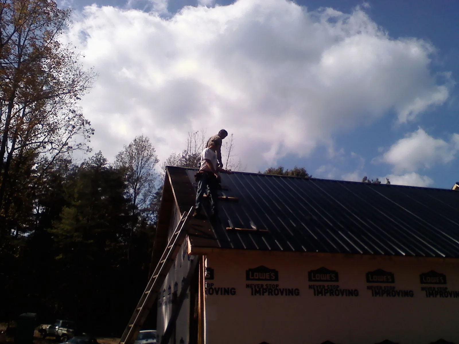 Roofer fastening dark metal panels high against a cloudy sky, from a Roof Inspection job in Merchantville