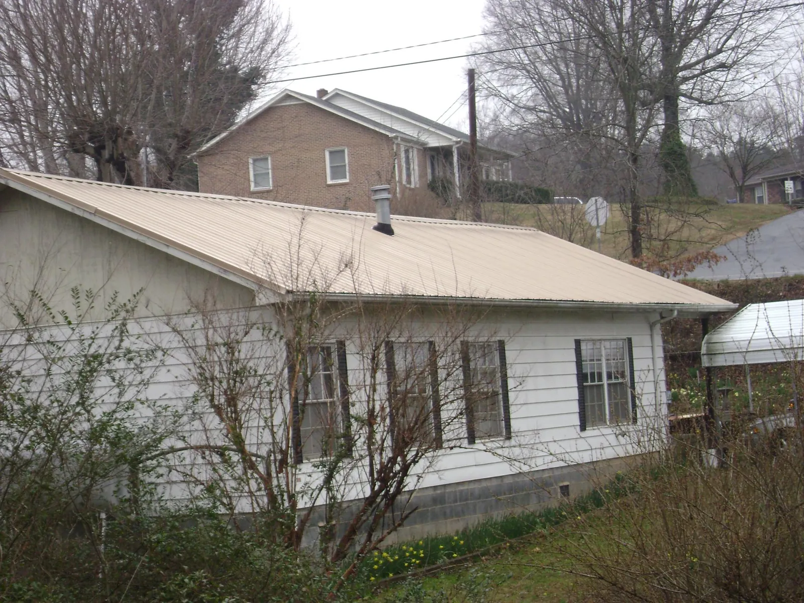 Tan metal roof on a white sided house set into a hillside — Commercial Roofing by Roofing Brothers in Merchantville